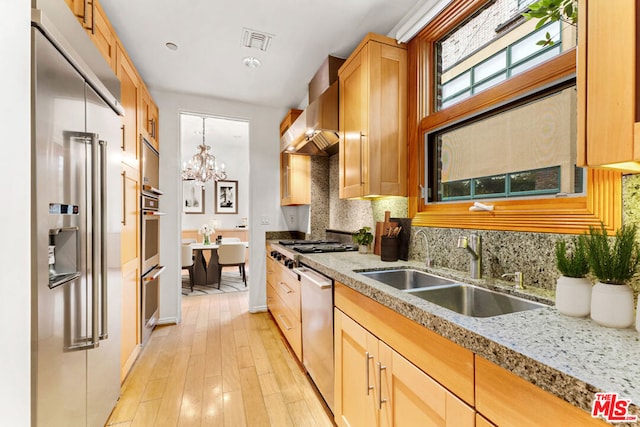 kitchen featuring appliances with stainless steel finishes, light wood-type flooring, tasteful backsplash, wall chimney exhaust hood, and sink