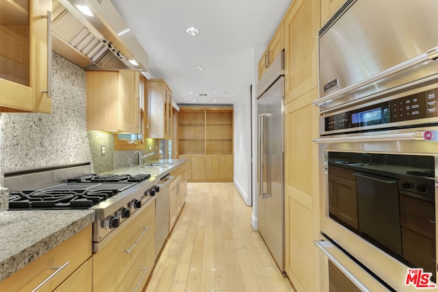 kitchen with light wood-type flooring, tasteful backsplash, wall chimney exhaust hood, stainless steel appliances, and sink