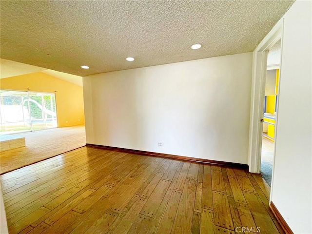 unfurnished room with hardwood / wood-style flooring, a textured ceiling, and vaulted ceiling