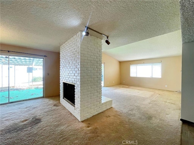 unfurnished living room featuring lofted ceiling, track lighting, carpet flooring, a fireplace, and a textured ceiling