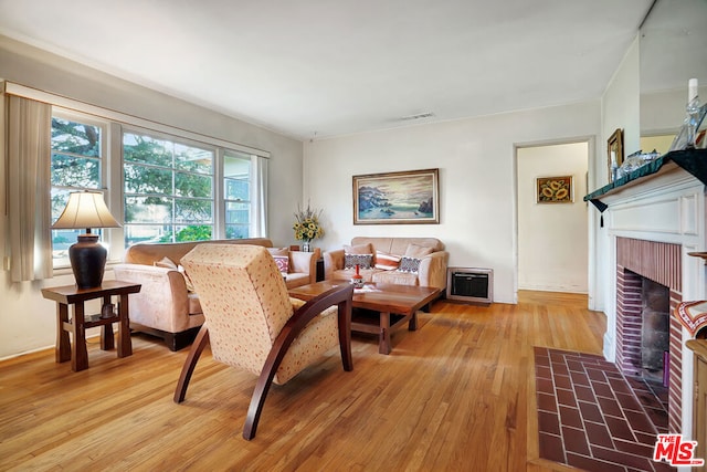 living room with a brick fireplace, heating unit, and light hardwood / wood-style flooring