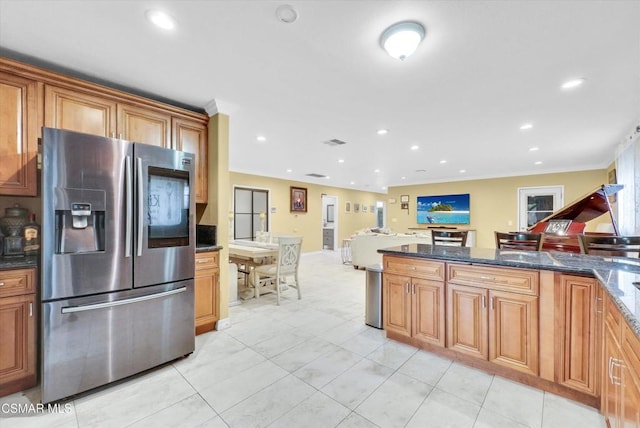 kitchen with crown molding, dark stone countertops, light tile patterned floors, and stainless steel refrigerator with ice dispenser