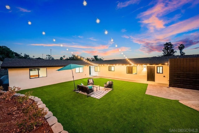 back house at dusk with a patio, outdoor lounge area, and a yard