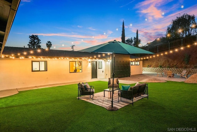 back house at dusk featuring outdoor lounge area, a patio area, and a lawn