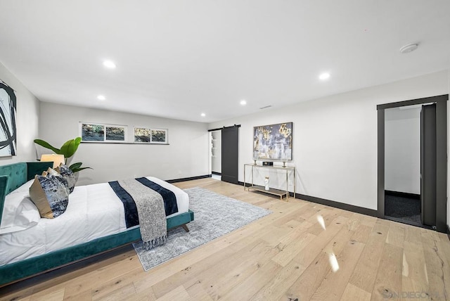 bedroom with a barn door and light hardwood / wood-style flooring