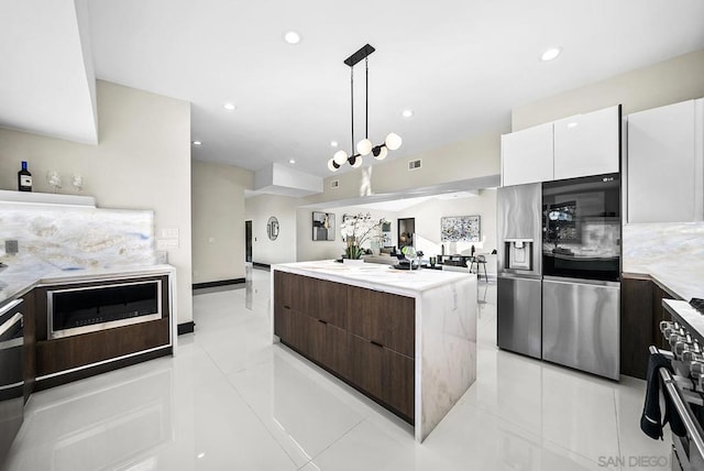 kitchen with pendant lighting, appliances with stainless steel finishes, white cabinetry, dark brown cabinetry, and a kitchen island