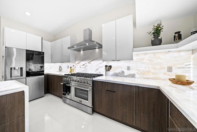 kitchen featuring tasteful backsplash, appliances with stainless steel finishes, wall chimney range hood, light stone countertops, and white cabinets