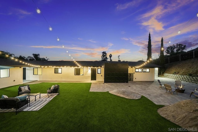 back house at dusk with a patio area and a lawn