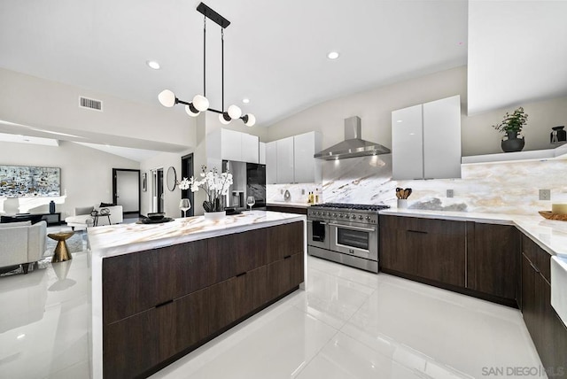 kitchen featuring vaulted ceiling, appliances with stainless steel finishes, white cabinetry, hanging light fixtures, and wall chimney range hood