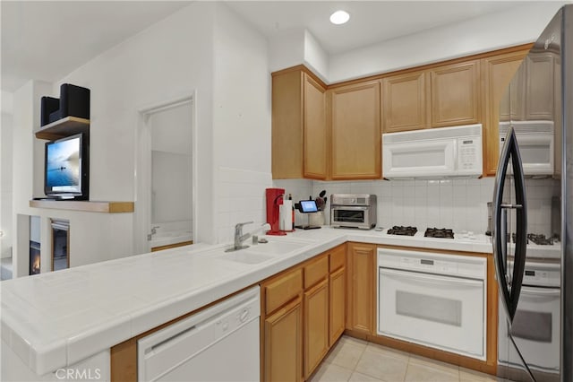 kitchen with tile countertops, kitchen peninsula, tasteful backsplash, white appliances, and sink