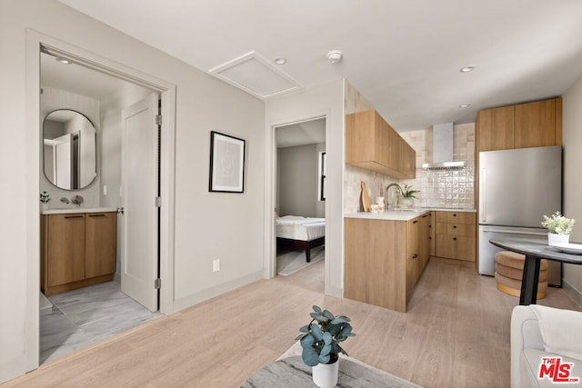 kitchen featuring stainless steel fridge, light wood-type flooring, backsplash, and wall chimney range hood