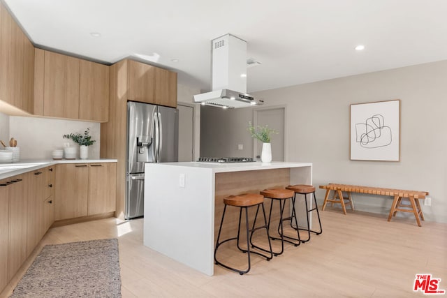 kitchen with light wood-type flooring, stainless steel appliances, island range hood, a center island, and a breakfast bar area