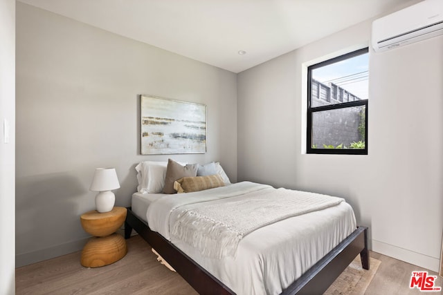 bedroom featuring light wood-type flooring and an AC wall unit