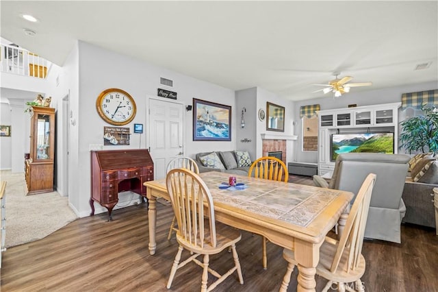 dining area featuring baseboard heating, ceiling fan, dark wood-type flooring, and a tiled fireplace