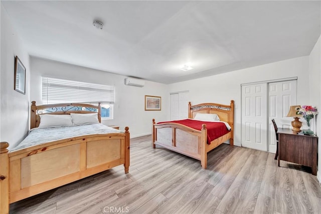 bedroom with two closets, light hardwood / wood-style floors, and a wall mounted AC