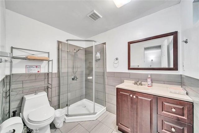 bathroom featuring toilet, a shower with door, tile walls, tile patterned floors, and vanity