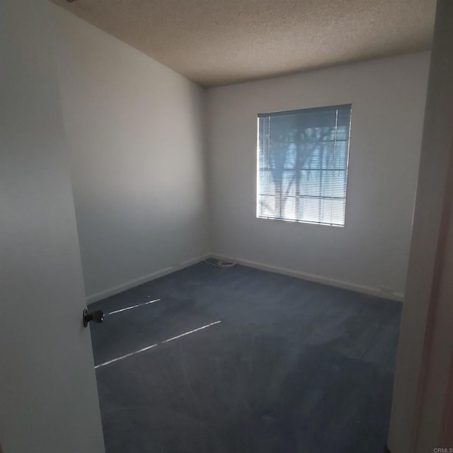 spare room featuring a textured ceiling and dark colored carpet