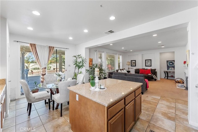 kitchen featuring light stone countertops, a center island, light colored carpet, and a healthy amount of sunlight