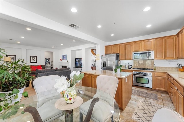 kitchen with light stone countertops, stainless steel appliances, light tile patterned floors, backsplash, and a kitchen island