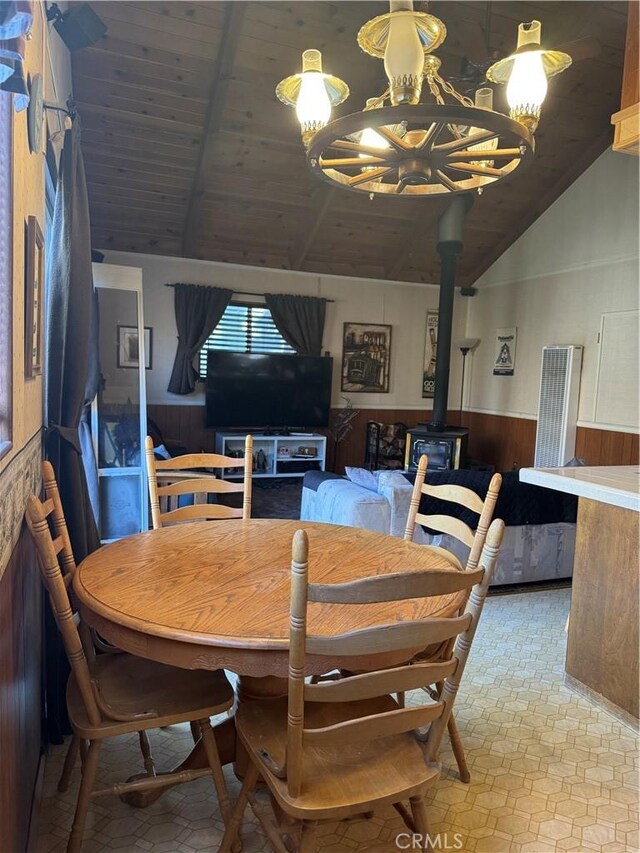 dining room with wood walls, an inviting chandelier, wood ceiling, lofted ceiling with beams, and a wood stove