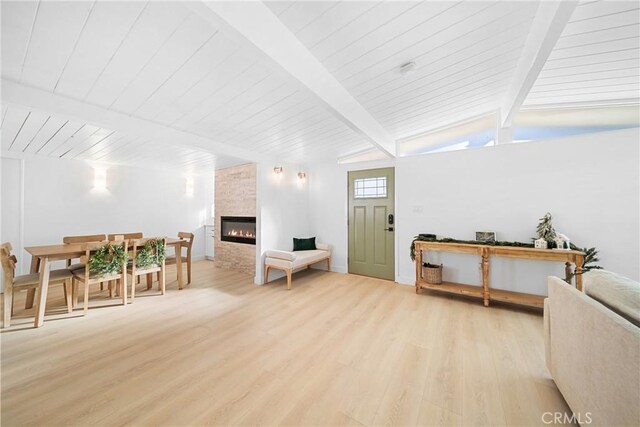 living room featuring vaulted ceiling with beams, a large fireplace, and light hardwood / wood-style flooring