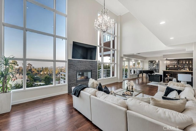 living room featuring a towering ceiling, a stone fireplace, plenty of natural light, and dark wood-type flooring