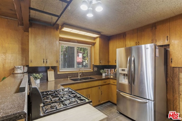 kitchen with light tile patterned flooring, sink, range with gas cooktop, stainless steel fridge with ice dispenser, and wooden walls