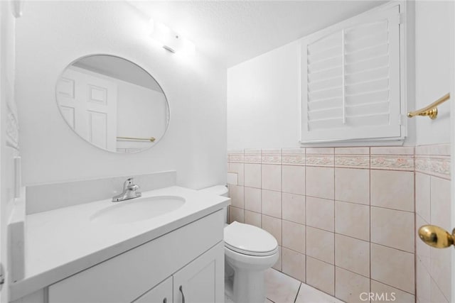 bathroom featuring tile patterned floors, vanity, toilet, and tile walls