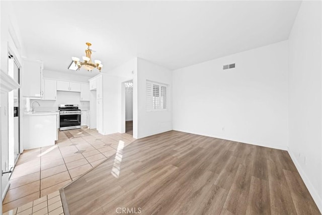 unfurnished living room featuring sink, a notable chandelier, and light wood-type flooring