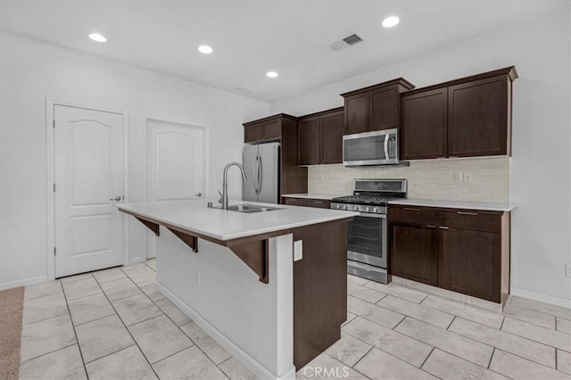 kitchen with a center island with sink, sink, decorative backsplash, appliances with stainless steel finishes, and dark brown cabinetry