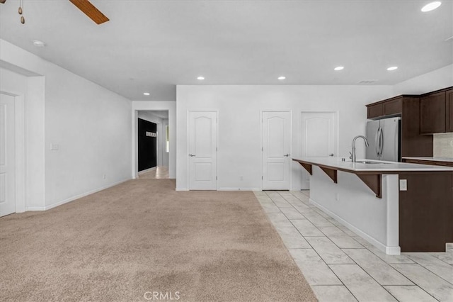 kitchen with stainless steel refrigerator, ceiling fan, a breakfast bar area, light carpet, and dark brown cabinets