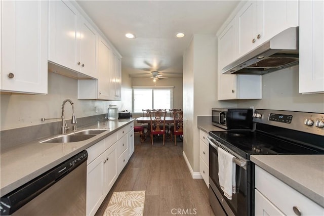 kitchen with light wood finished floors, white cabinets, stainless steel appliances, under cabinet range hood, and a sink