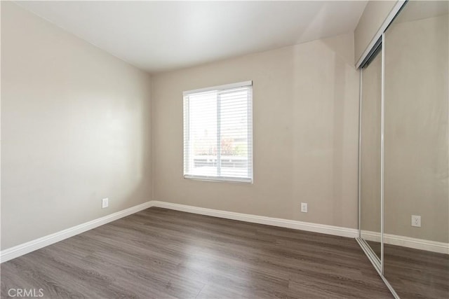 unfurnished bedroom with dark wood-style floors, a closet, and baseboards