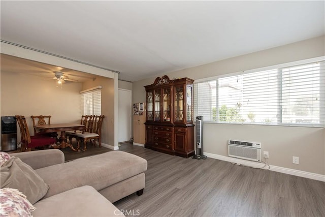 living area featuring ceiling fan, a wall mounted air conditioner, wood finished floors, and baseboards