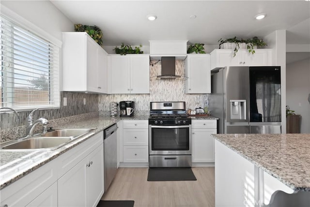 kitchen with light stone counters, stainless steel appliances, sink, wall chimney range hood, and white cabinets