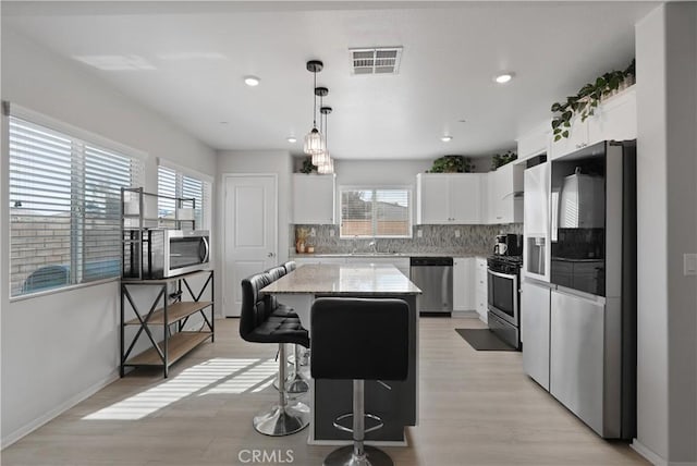 kitchen with pendant lighting, a wealth of natural light, a kitchen island, and appliances with stainless steel finishes