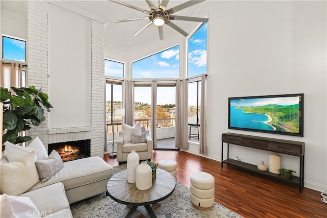 living room with ceiling fan, dark wood-type flooring, a high ceiling, a fireplace, and ornamental molding