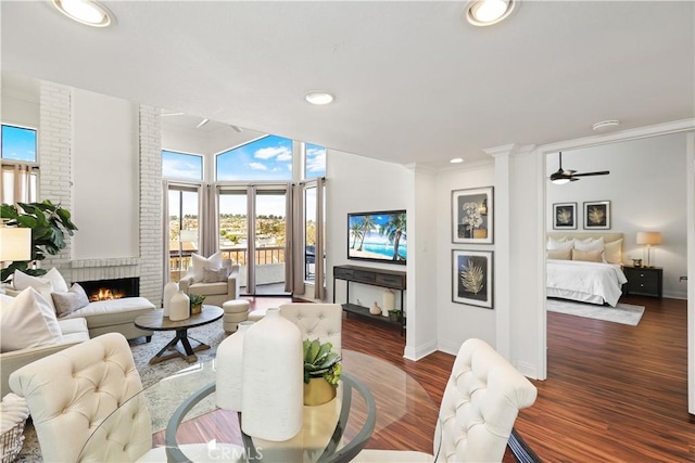 living room featuring a fireplace, ceiling fan, ornamental molding, and dark wood-type flooring