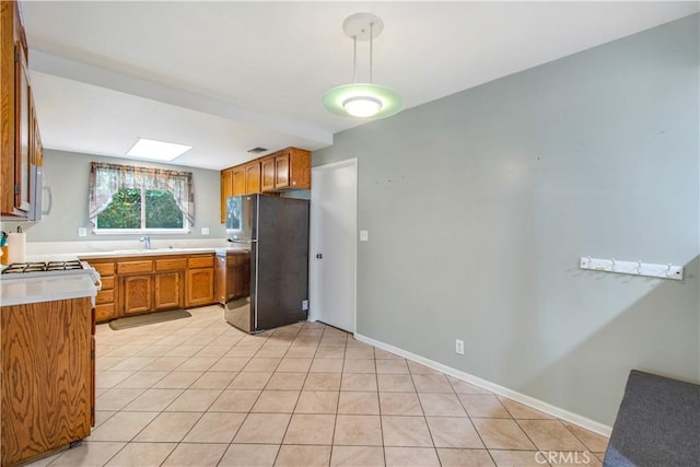 kitchen featuring stainless steel fridge, light tile patterned flooring, sink, and a skylight