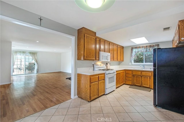 kitchen featuring a skylight, sink, light hardwood / wood-style floors, and white appliances