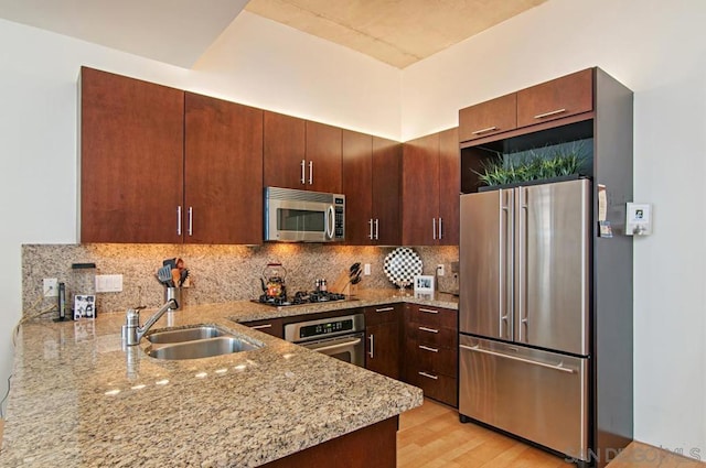 kitchen featuring sink, light hardwood / wood-style flooring, light stone countertops, appliances with stainless steel finishes, and kitchen peninsula