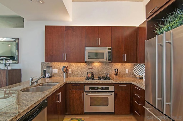 kitchen with kitchen peninsula, tasteful backsplash, light stone counters, stainless steel appliances, and sink