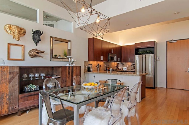 dining area featuring light wood-type flooring, a high ceiling, and a chandelier