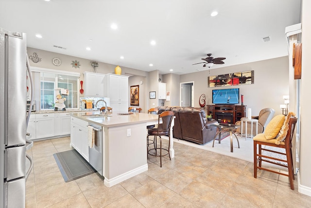 kitchen featuring ceiling fan, stainless steel appliances, a kitchen bar, a kitchen island with sink, and white cabinets