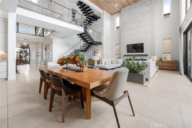 tiled dining area with a towering ceiling, a fireplace, and wood ceiling