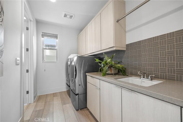 laundry area featuring cabinets, independent washer and dryer, sink, and light hardwood / wood-style flooring