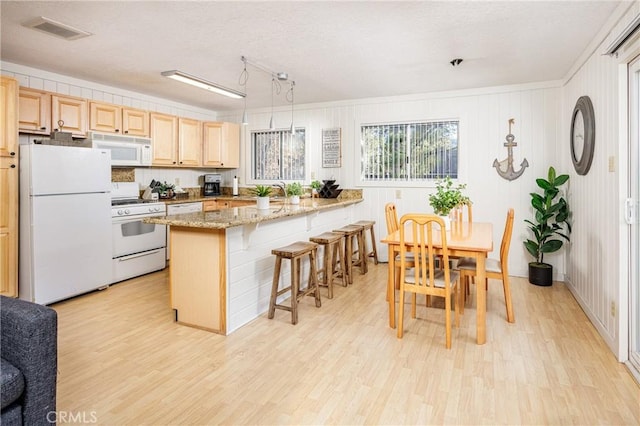 kitchen featuring a kitchen breakfast bar, white appliances, and light hardwood / wood-style flooring