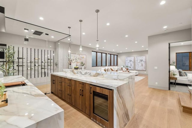 kitchen with pendant lighting, sink, a spacious island, wine cooler, and light stone countertops