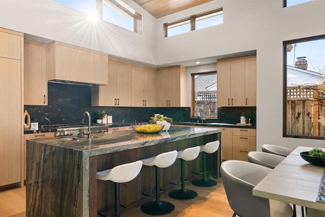 kitchen featuring a kitchen island with sink, a towering ceiling, light hardwood / wood-style floors, and light brown cabinets