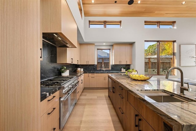 kitchen featuring sink, wood ceiling, light wood-type flooring, light brown cabinets, and wall chimney range hood